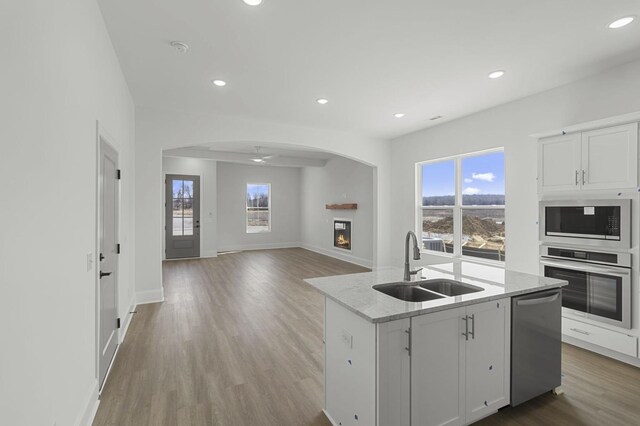 166 Oasis Dr, La Vergne, TN 37086 - kitchen featuring stainless steel appliances, arched walkways, a lit fireplace, a sink, and light wood-type flooring