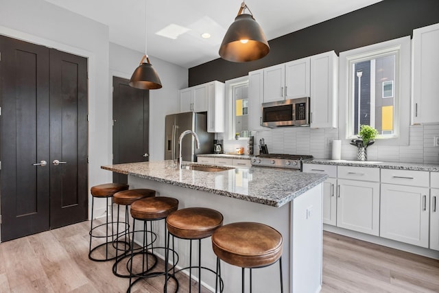 kitchen with a sink, stainless steel appliances, tasteful backsplash, and light wood finished floors