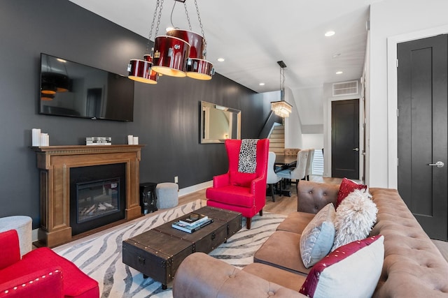 living area with visible vents, stairs, wood finished floors, recessed lighting, and a glass covered fireplace