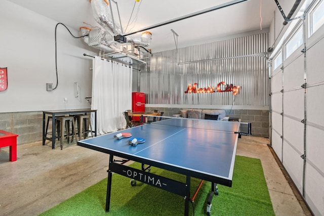 recreation room with concrete block wall, concrete flooring, and a garage