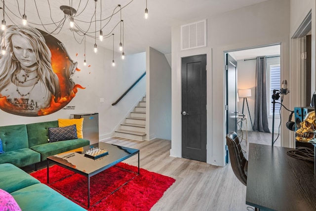 living area with visible vents, an inviting chandelier, stairway, and wood finished floors