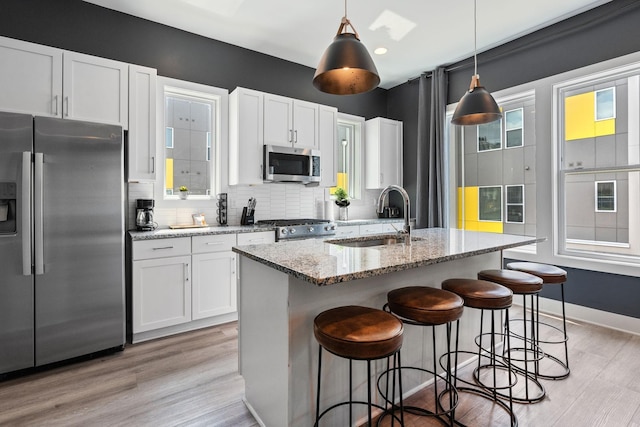 kitchen featuring white cabinets, a kitchen breakfast bar, appliances with stainless steel finishes, a sink, and backsplash