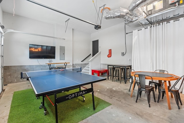 rec room with concrete block wall, concrete flooring, and electric panel