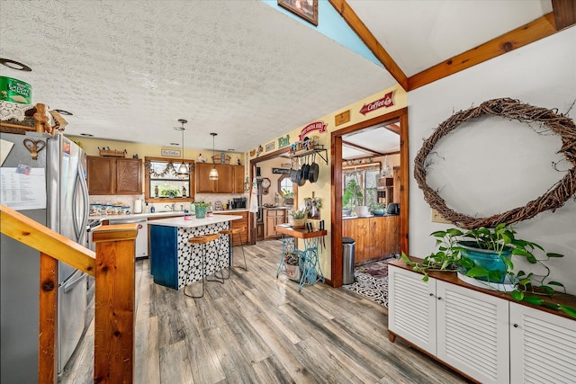 kitchen with light countertops, a textured ceiling, light wood-style floors, freestanding refrigerator, and brown cabinets