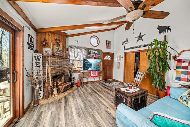 living room featuring a ceiling fan, vaulted ceiling with beams, wood finished floors, a brick fireplace, and baseboards