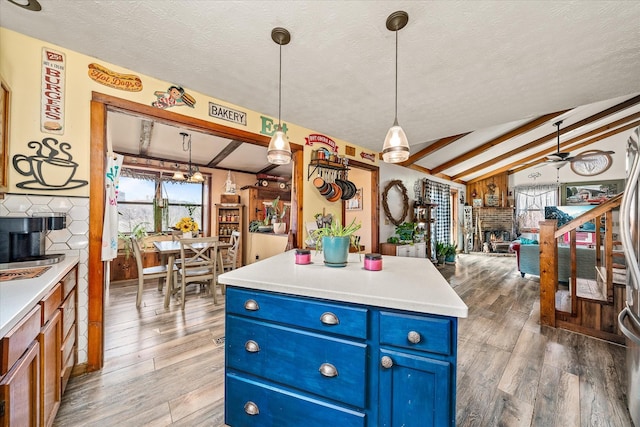 kitchen with open floor plan, vaulted ceiling with beams, blue cabinetry, and light wood finished floors