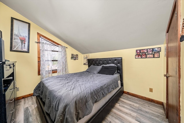 bedroom with baseboards, lofted ceiling, and wood finished floors