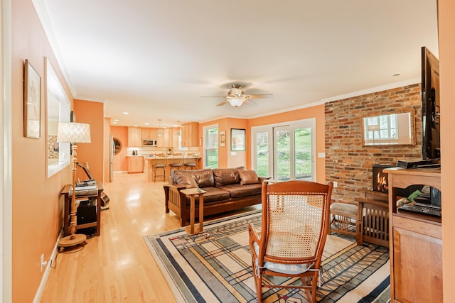 living area featuring crown molding, baseboards, ceiling fan, light wood-style floors, and brick wall