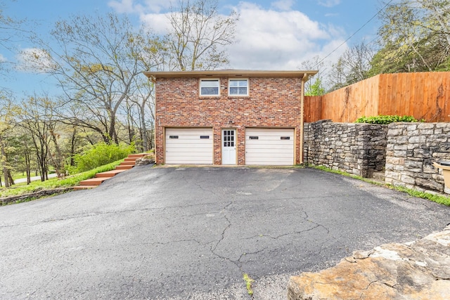 exterior space featuring driveway, brick siding, fence, and an attached garage