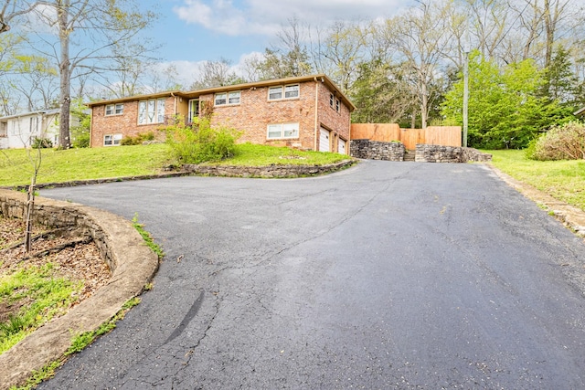 view of front of home featuring fence, a garage, a front yard, brick siding, and driveway