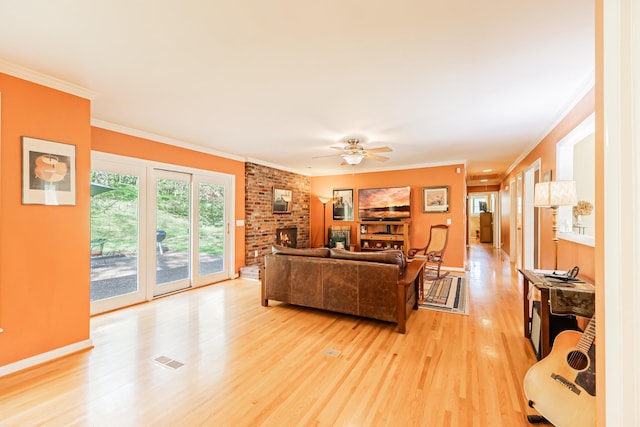 living area featuring crown molding, a brick fireplace, light wood-style flooring, visible vents, and ceiling fan