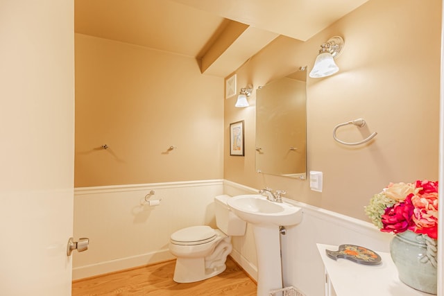 half bathroom with a wainscoted wall, toilet, a sink, wood finished floors, and visible vents