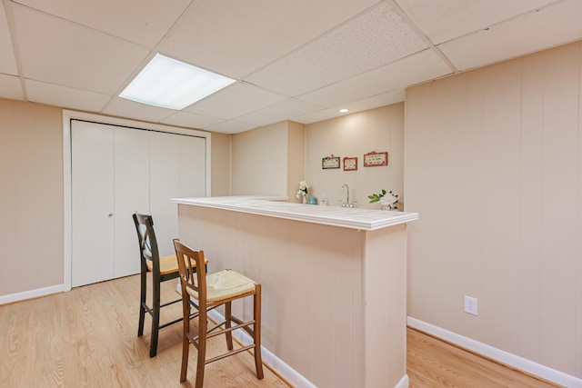 bar with bar area, baseboards, a sink, light wood finished floors, and a paneled ceiling