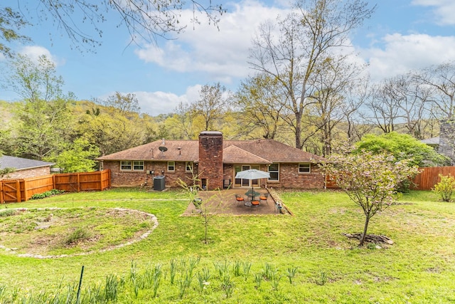 rear view of house with a patio, a chimney, a fenced backyard, brick siding, and a yard
