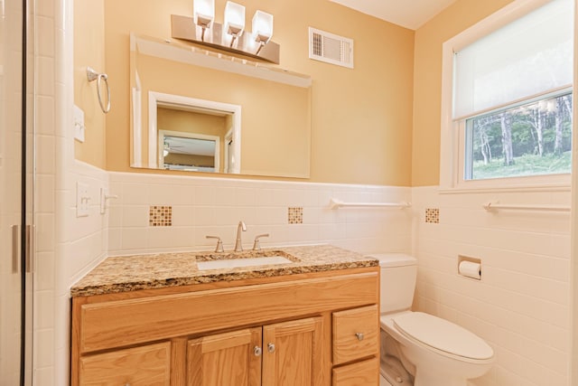 bathroom with tile walls, a wainscoted wall, visible vents, toilet, and vanity