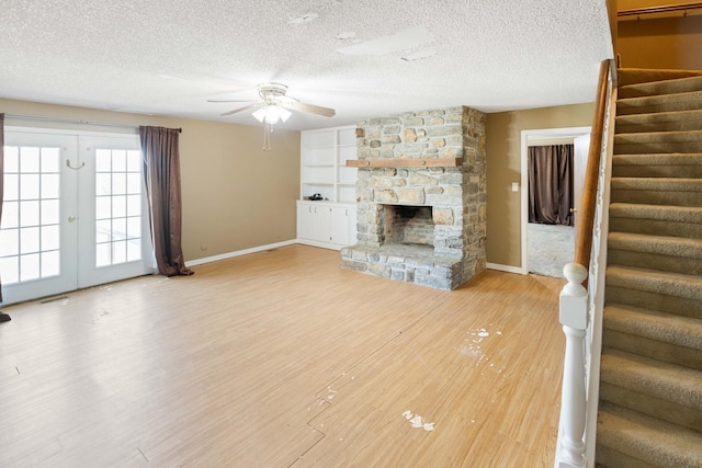 unfurnished living room with stairs, french doors, a fireplace, light wood-type flooring, and ceiling fan