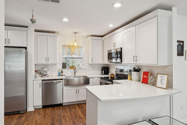 kitchen featuring stainless steel appliances, a sink, a peninsula, white cabinetry, and light countertops
