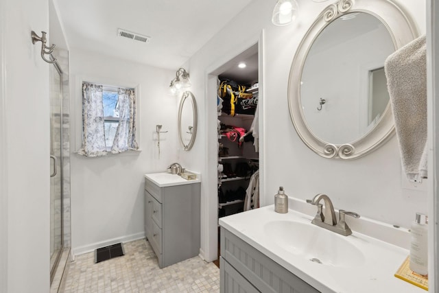 bathroom with two vanities, a walk in closet, a shower with shower door, and baseboards