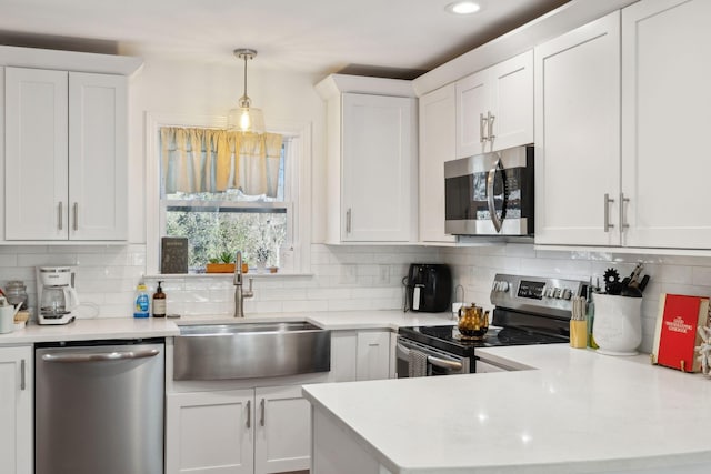 kitchen featuring appliances with stainless steel finishes, a sink, a peninsula, white cabinets, and light countertops