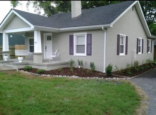 single story home with a front lawn, a chimney, stucco siding, and a porch