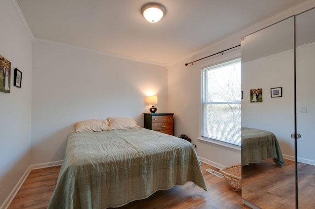 bedroom with baseboards, visible vents, wood finished floors, and crown molding