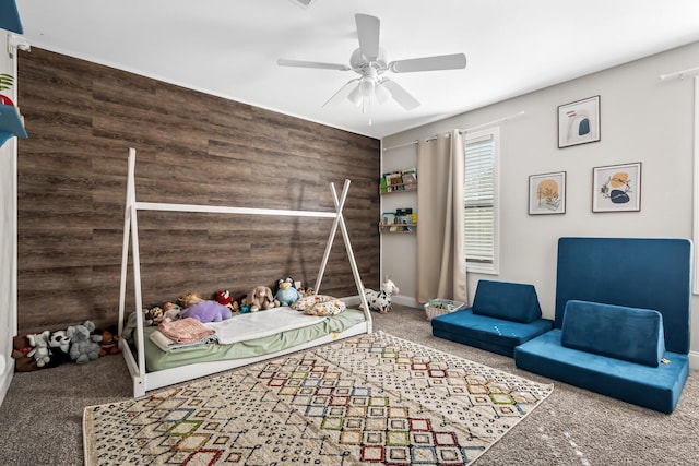 carpeted bedroom featuring wood walls and a ceiling fan