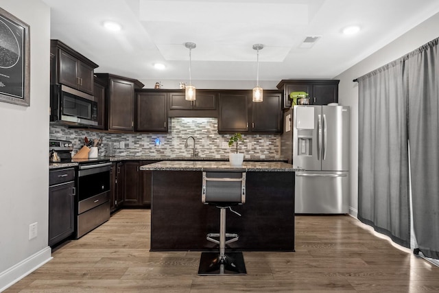 kitchen with a sink, light wood-style floors, light stone countertops, dark brown cabinets, and appliances with stainless steel finishes