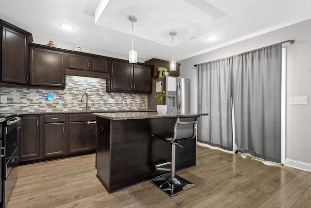 kitchen with dark stone countertops, a sink, stainless steel fridge, and light wood finished floors
