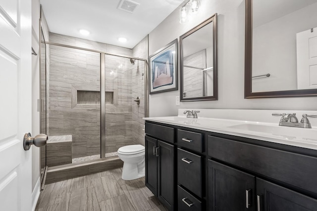 bathroom featuring toilet, a shower stall, a sink, visible vents, and double vanity