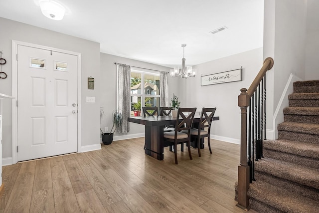 dining area with stairs, a chandelier, light wood finished floors, baseboards, and visible vents