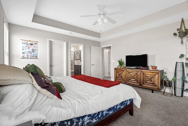 carpeted bedroom featuring a ceiling fan, a raised ceiling, and ensuite bath