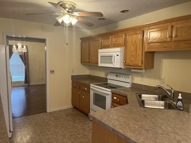 kitchen featuring white appliances, brown cabinets, dark countertops, a sink, and ceiling fan with notable chandelier