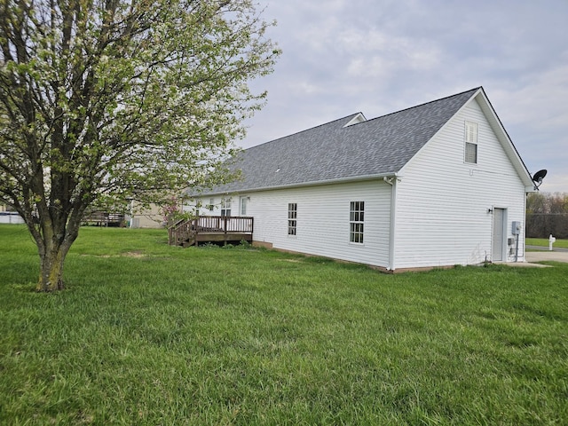 exterior space with a shingled roof, a deck, and a lawn