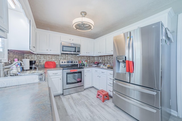 kitchen featuring white cabinets, a sink, light wood-type flooring, appliances with stainless steel finishes, and decorative backsplash