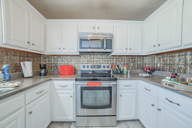 kitchen featuring white cabinetry, backsplash, appliances with stainless steel finishes, and light wood-style floors