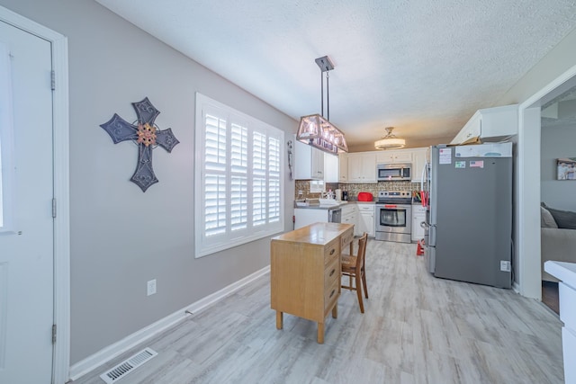 dining space with light wood finished floors, visible vents, a textured ceiling, and baseboards