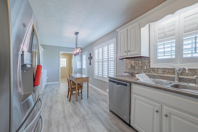 kitchen with tasteful backsplash, light wood-style flooring, white cabinets, appliances with stainless steel finishes, and a sink