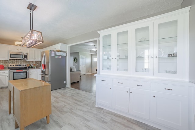 kitchen with glass insert cabinets, light wood-type flooring, white cabinetry, a chandelier, and appliances with stainless steel finishes