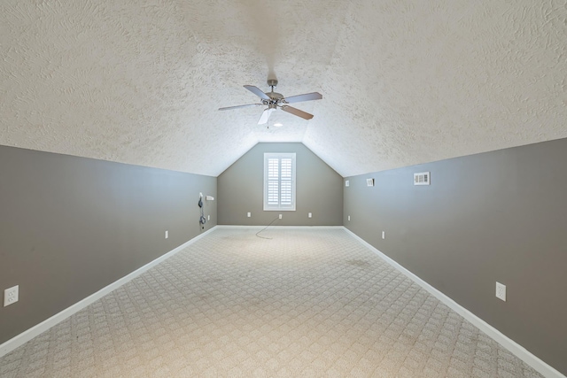 additional living space featuring a textured ceiling, a ceiling fan, visible vents, lofted ceiling, and baseboards