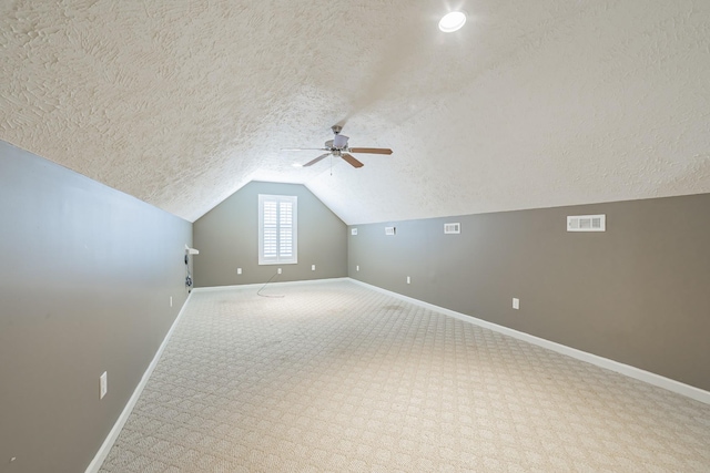 additional living space featuring visible vents, baseboards, ceiling fan, a textured ceiling, and vaulted ceiling