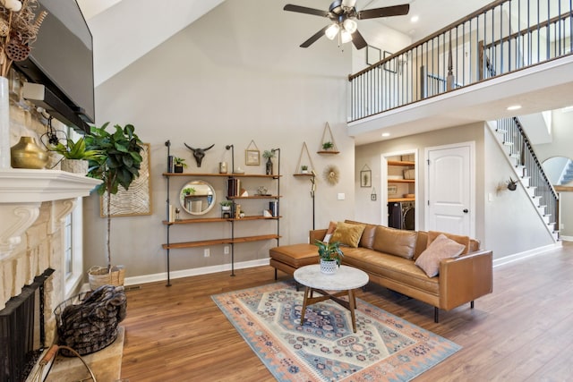 living area with stairway, high vaulted ceiling, ceiling fan, a fireplace, and baseboards