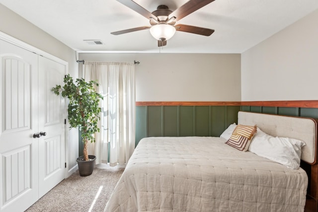 bedroom featuring a closet, ceiling fan, carpet floors, a wainscoted wall, and visible vents
