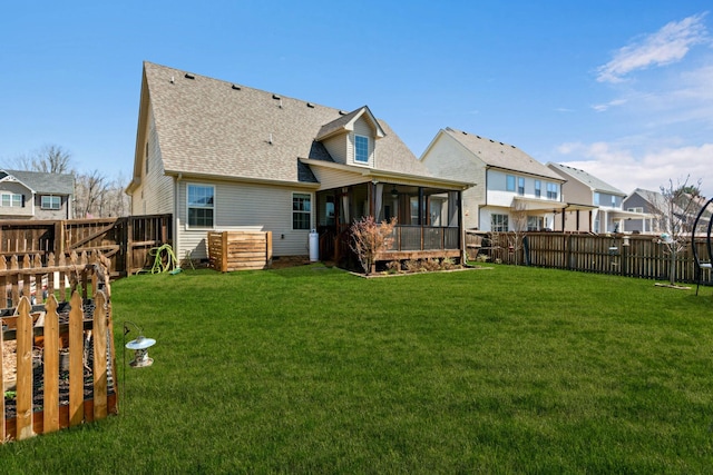 rear view of house featuring a fenced backyard, a sunroom, and a yard