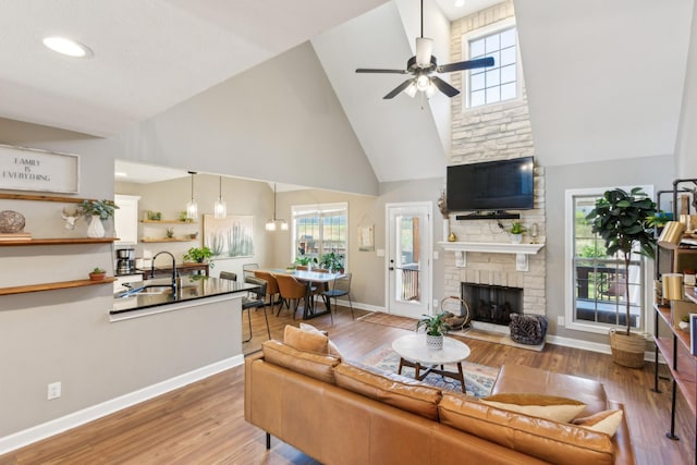 living area featuring wood finished floors, a brick fireplace, high vaulted ceiling, and ceiling fan