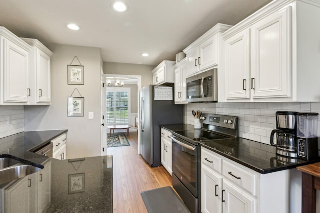 kitchen with dark stone countertops, white cabinetry, light wood-style flooring, backsplash, and appliances with stainless steel finishes