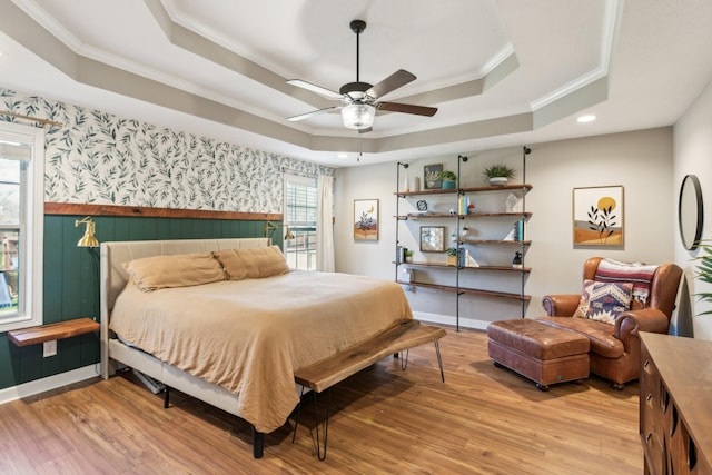 bedroom with crown molding, a wainscoted wall, a tray ceiling, and light wood-type flooring