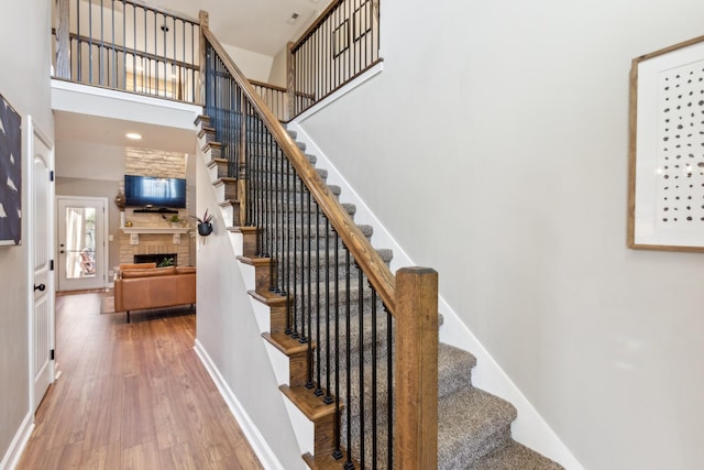 staircase featuring hardwood / wood-style flooring, baseboards, a high ceiling, and a fireplace
