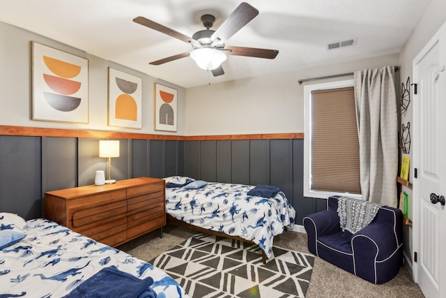 bedroom featuring carpet, visible vents, a wainscoted wall, and ceiling fan