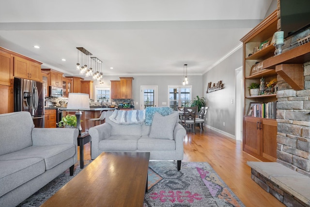 living area featuring light wood-style flooring, plenty of natural light, ornamental molding, and baseboards