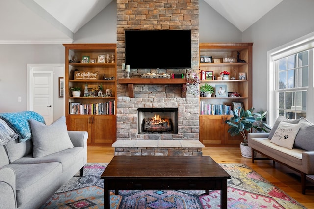 living room with a stone fireplace, vaulted ceiling, and light wood-style floors
